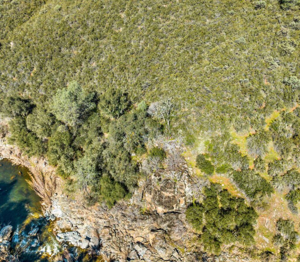 An aerial shot of undeveloped land with a thick foliage of trees, a creek and lots of rock outcroppings.