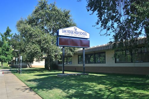 This photo shows the main school sign for Oak Ridge High School in El Dorado Hills, California. There is green grass, trees and blue sky.
